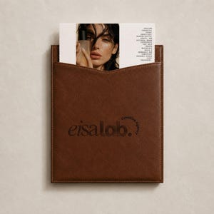May include: A brown leather document holder featuring the embossed text eisalab. Creative Agency. A white card is tucked inside, displaying a photograph of a person holding a bottle and text detailing services for building brand experiences.