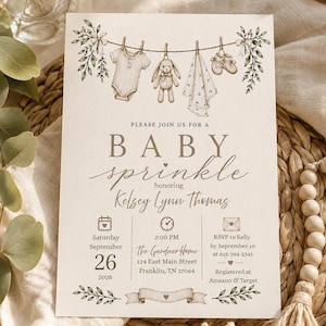Peut inclure: Une carte d'invitation crème pour une fête prénatale avec une illustration de corde à linge portant un body, un lapin en peluche, une couverture et des chaussons. Le texte indique : Please join us for a baby sprinkle honoring Kelsey Lynn Thomas, Saturday September 26 2026, 2:00 PM, The Gardner Home, 124 East Main Street, Franklin, TN 37064, RSVP to Kelly by September 10 at 615-394-2341, Registered at Amazon & Target.