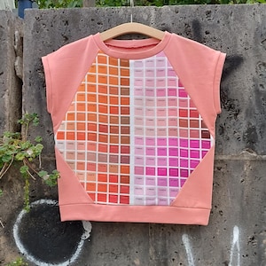 Könnte beinhalten: Ein kurzärmliges Shirt in Korallenfarbe mit einem Farbmuster auf der Vorderseite. Die Farbkarte zeigt eine Reihe von Farben von Orange bis Rosa.