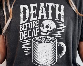 Może przedstawiać: Ciemnoszara koszulka z białym nadrukiem. Grafika przedstawia napis "DEATH BEFORE DECAF" nad szkieletem w kubku do kawy. Koszulka ma okrągły dekolt.