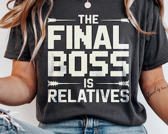 May include: Black heather t-shirt with the text "THE FINAL BOSS IS RELATIVES" in a white, pixelated font. The shirt has a crew neck and short sleeves. The words "BLACK HEATHER" are printed at the bottom of the shirt.