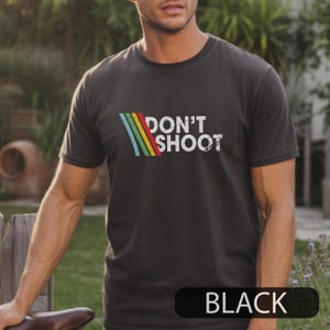 May include: Black crew neck t with the text "DON'T SHOOT" in white, and a colourful striped design. The word "BLACK" is displayed at the bottom of the shirt.