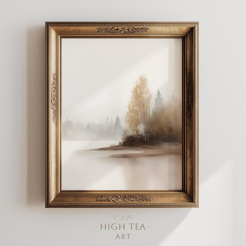Op de afbeelding: Een ingelijste landschapskunstafdruk met een serene, mistige meerzicht met bomen in bruin- en grijstinten. Het kunstwerk is ingesloten in een goudkleurige, sierlijke lijst. De tekst "HIGH TEA ART" staat onderaan.