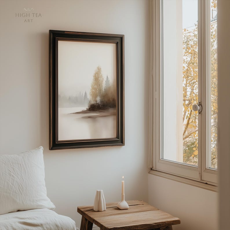 Op de afbeelding: Een ingelijste landschapskunstafdruk met een serene meerzicht met bomen en een mistige sfeer. Het kunstwerk bevindt zich in een donkere houten lijst en hangt aan een witte muur. Een kleine houten tafel bevat een kaars en een vaas. De tekst "HIGH TEA ART" staat in de linkerbovenhoek.