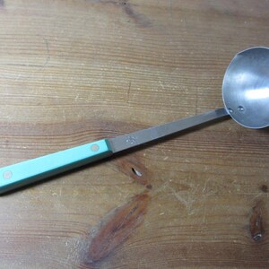 May include: A stainless steel ladle with a light blue handle. The ladle has a round bowl and a long, flat handle. The handle is light blue with two small, round, silver rivets. The ladle is designed for serving soups, stews, and sauces.