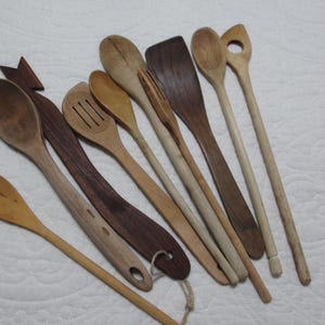 May include: A selection of wooden kitchen utensils, including spoons and spatulas. The spoons and spatulas are in various shades of brown. Some have holes for hanging. The utensils are arranged on a white surface, ideal for cooking and baking.