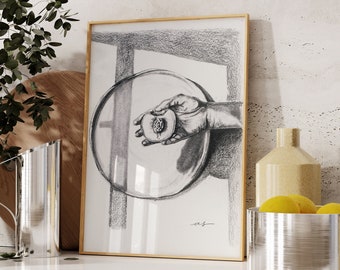 May include: A black and white pencil drawing of a hand holding a peach inside a round, reflective object. The drawing is framed in a gold frame and is hanging on a white wall.
