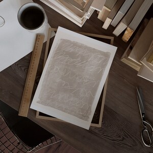 May include: A framed abstract art print with a beige background and white scribbles. The print is in a wooden frame.