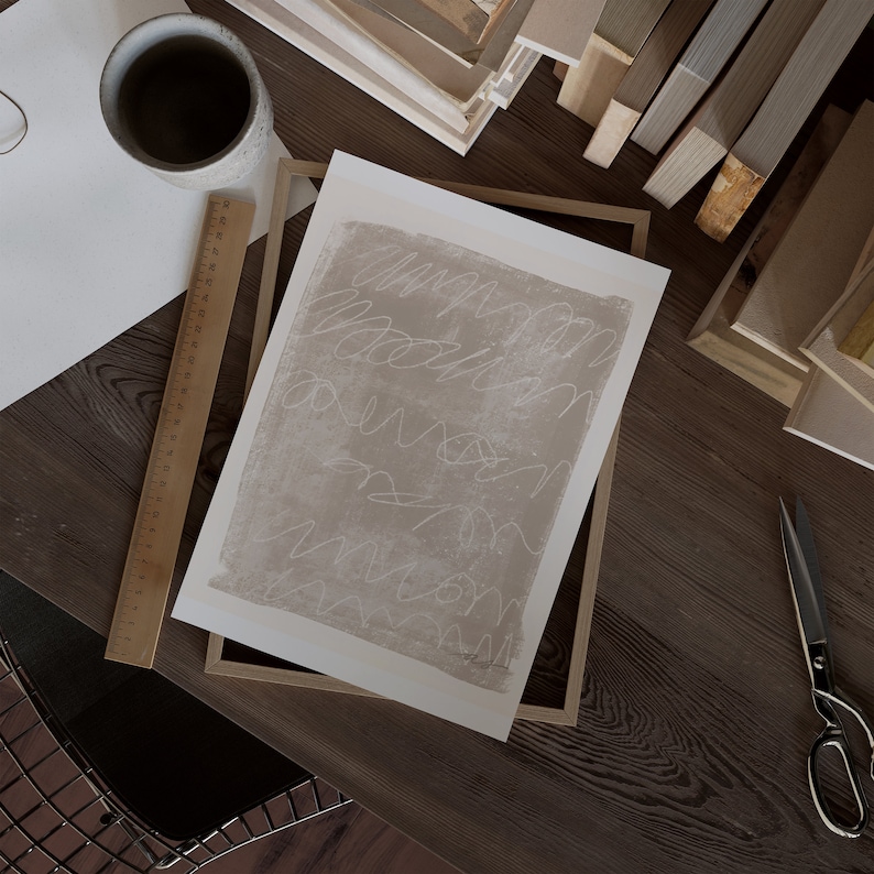 May include: A framed abstract art print with a beige background and white scribbles. The print is in a wooden frame.