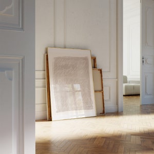 May include: A framed abstract art print with a light brown background and white lines. The print is hanging on a white wall in a room with wooden floors.