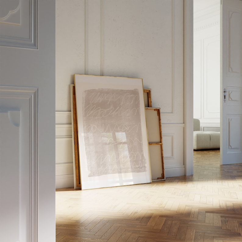May include: A framed abstract art print with a light brown background and white lines. The print is hanging on a white wall in a room with wooden floors.