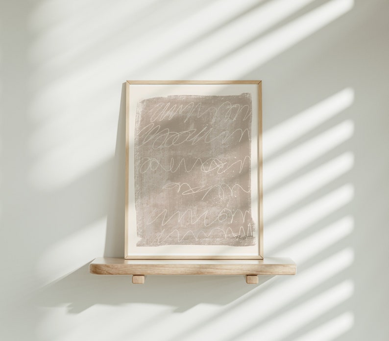 May include: A framed abstract print with a light brown background and white lines. The print is on a wooden shelf against a white wall.