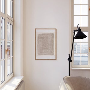 May include: A framed abstract art print with a beige background and white lines. The print is hanging on a white wall in a room with a large window and a white couch.