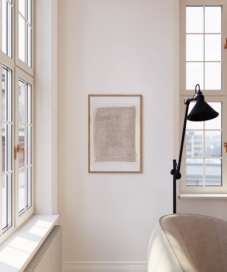 May include: A framed abstract art print with a beige background and white lines. The print is hanging on a white wall in a room with a large window and a white couch.