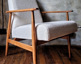 May include: A white armchair with a textured fabric upholstery and a wooden frame. The chair has a simple design with four legs and a single armrest. The chair is sitting on a wooden floor.
