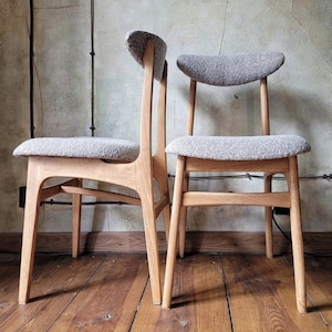 Może przedstawiać: Dwa drewniane krzesła z szarymi siedziskami z tkaniny. Krzesła mają nowoczesny design z połowy wieku z zakrzywionymi oparciami i pochylonymi nogami.