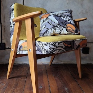 Può includere: Una poltrona gialla con gambe in legno e un cuscino con motivo tucano. La poltrona è rivestita in tessuto giallo con motivo tucano.