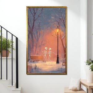 Puede incluir: Una impresión artística enmarcada representa a dos esqueletos tomados de la mano bajo una farola en un parque nevado. La obra de arte presenta un cálido resplandor dorado de la lámpara sobre un fondo de árboles y un banco, todo dentro de un marco dorado.