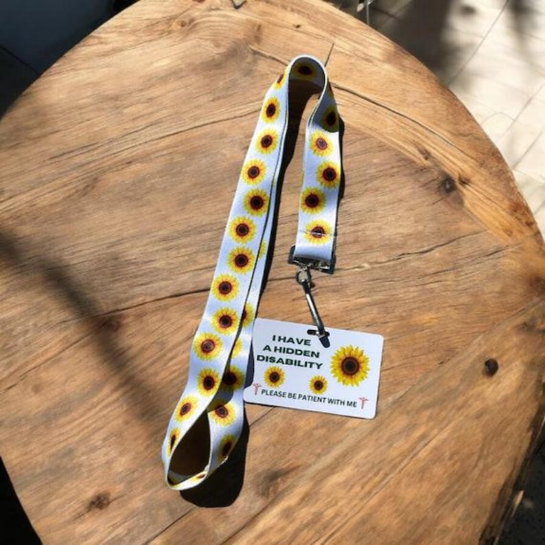 May include: White lanyard with a sunflower pattern and a white card attached. The card reads "I have a hidden disability. Please be patient with me."