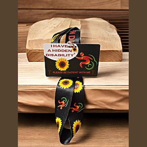 May include: Black lanyard with sunflowers and a red, green, and yellow symbol. A white card attached to the lanyard reads "I have a hidden disability. Please be patient with me".