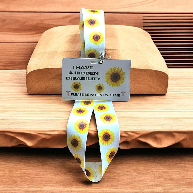 May include: A white lanyard with a sunflower pattern and a white card attached to it. The card reads "I have a hidden disability. Please be patient with me." and has a sunflower graphic on it.