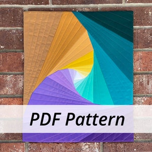 May include: A PDF pattern for a colorful quilt with a spiral design in shades of purple, teal, yellow, and brown. The quilt is displayed against a brick wall.