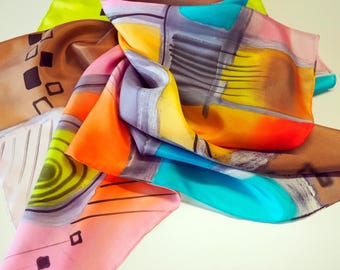 Puede incluir: Un pañuelo de seda colorido con un diseño abstracto. El pañuelo presenta una variedad de colores, incluyendo rosa, naranja, amarillo, azul y marrón. El diseño incluye formas geométricas y líneas. El pañuelo está doblado, mostrando sus vibrantes colores y patrones.