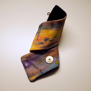 May include: A colorful fabric neck warmer with a button closure. The fabric has a geometric pattern with shades of yellow, orange, blue, and purple.