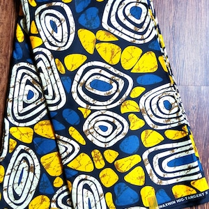 May include: Two pieces of fabric with a black background and a pattern of white circles, yellow ovals, and blue shapes. The fabric has the text "VERITABLE WAX BLOCK PRINT" and "WAXWIN HIG-TARGERT W" printed on it.