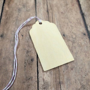 May include: A blank wooden gift tag with a hole at the top and a white and purple twine attached.