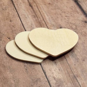 May include: Three unfinished wooden heart shapes stacked on top of each other on a brown wooden surface.