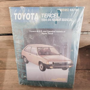 May include: A Toyota Tercel 1984-94 repair manual. The cover is blue and features an image of a beige Tercel hatchback. Text on the cover includes "TOYOTA TERCEL 1984-94 REPAIR MANUAL" and "WIRING AND VACUUM DIAGRAMS."