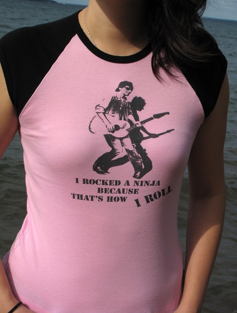 May include: Pink and black raglan t-shirt with a graphic of a guitarist and the text "I rocked a ninja because that's how I roll". The shirt is made of a soft material.