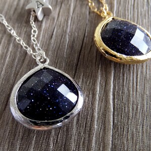 Pode incluir: Dois colares com pingentes facetados azul escuro. Um pingente &eacute; cravejado em prata, o outro em ouro. Uma corrente de prata com um berloque de estrela &eacute; presa a um colar. Os pingentes t&ecirc;m uma apar&ecirc;ncia estrelada e brilhante.
