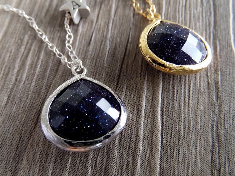 Pode incluir: Dois colares com pingentes facetados azul escuro. Um pingente &eacute; cravejado em prata, o outro em ouro. Uma corrente de prata com um berloque de estrela &eacute; presa a um colar. Os pingentes t&ecirc;m uma apar&ecirc;ncia estrelada e brilhante.