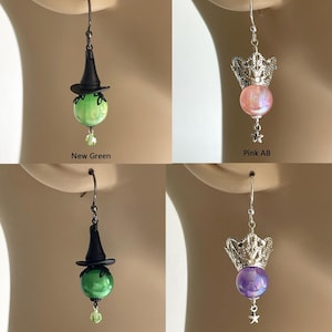 May include: Four pairs of dangle earrings. Two pairs feature a witch hat design with green orbs. The other two pairs have a crown design with pink or purple orbs. Each earring has a small star charm.