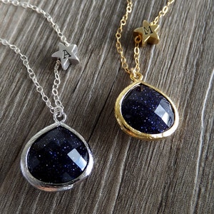 Pode incluir: Dois colares com pingentes em forma de gota. Um tem corrente e moldura prateadas, o outro corrente e moldura douradas. Ambos os pingentes s&atilde;o azul escuro com inclus&otilde;es brilhantes. Cada colar tem um pequeno pingente de estrela com uma letra.