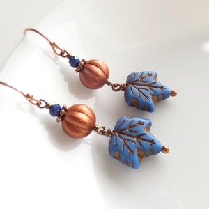 May include: A pair of copper dangle earrings with blue glass leaves and copper pumpkin beads. The leaves have a gold metallic finish.