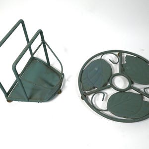 Może przedstawiać: Dwa elementy dekoracji domu z metalu w kolorze morskim. Jednym z nich jest kwadratowy serwetnik z górą w kształcie rombu. Drugi to okrągła podstawka z motywem liści. Oba elementy mają postarzany, vintage wygląd.