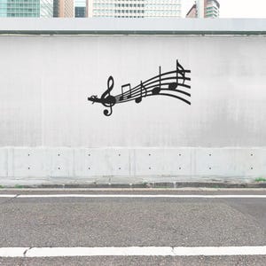以下が含まれることがあります： 白い壁に黒い金属製の音楽記号のデザインが取り付けられています。デザインには、ト音記号と音符が含まれています。