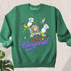 May include: Green sweatshirt with a cartoon image of Buzz Lightyear from Toy Story flying with the text "And Beyond".