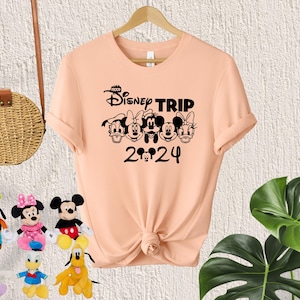 Puede incluir: Camiseta de color melocot&oacute;n con un gr&aacute;fico negro de Mickey Mouse y sus amigos. El gr&aacute;fico dice "Disney Trip 2024".