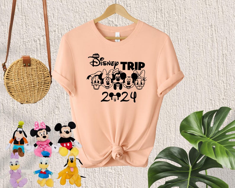 Puede incluir: Camiseta de color melocot&oacute;n con un gr&aacute;fico negro de Mickey Mouse y sus amigos. El gr&aacute;fico dice "Disney Trip 2024".