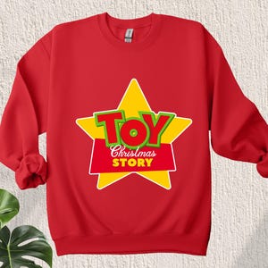Puede incluir: Sudadera roja con una estrella amarilla y las palabras "Toy Story" en letras verdes y rojas.