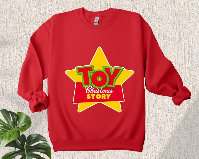 Puede incluir: Sudadera roja con una estrella amarilla y las palabras "Toy Story" en letras verdes y rojas.