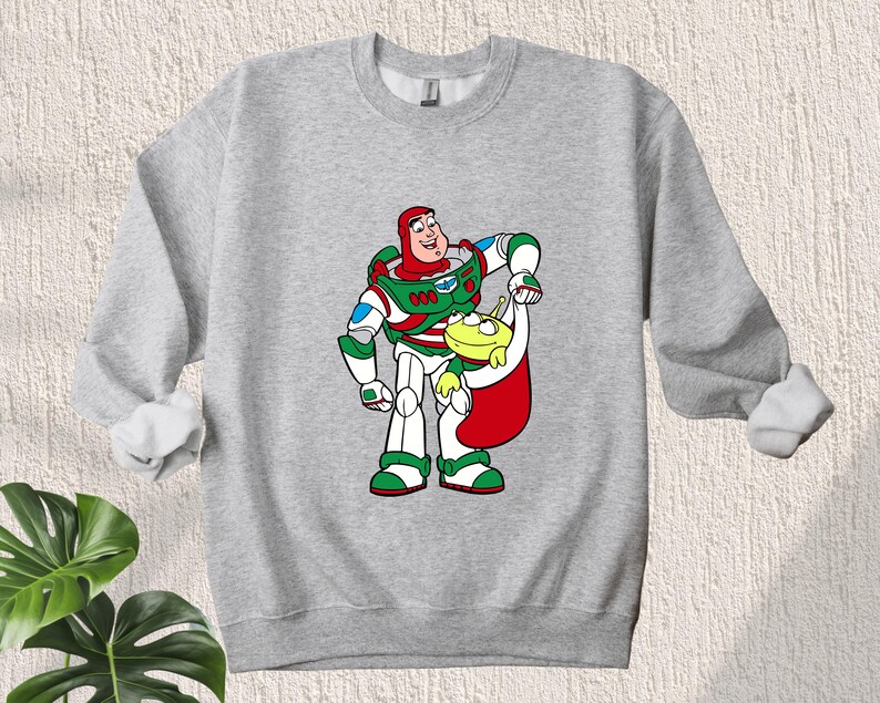 Puede incluir: Una sudadera gris con una imagen navide&ntilde;a de Buzz Lightyear de Toy Story con un gorro de Pap&aacute; Noel y sosteniendo un extraterrestre verde.