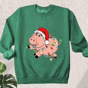 May include: Green Christmas sweatshirt with a cartoon pig wearing a Santa hat and wrapped in Christmas lights.