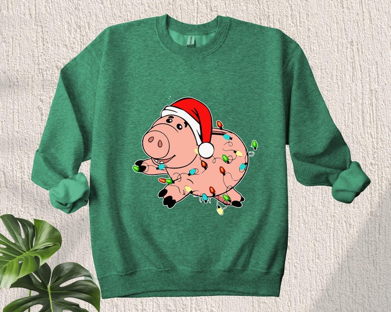 May include: Green Christmas sweatshirt with a cartoon pig wearing a Santa hat and wrapped in Christmas lights.