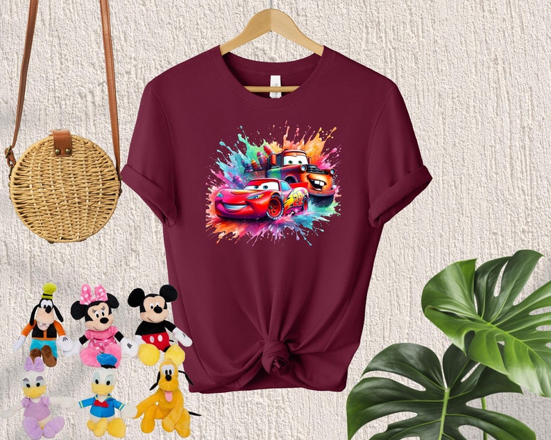 May include: Burgundy t-shirt with a colorful graphic of cartoon cars from the movie Cars. The graphic features Lightning McQueen, Mater, and a red race car.