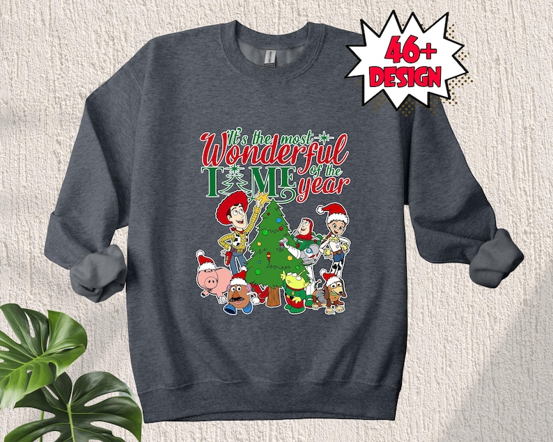 May include: A dark grey sweatshirt with a Christmas-themed design featuring the Toy Story characters Woody, Buzz Lightyear, and others. The text on the sweatshirt reads "It's the most wonderful time of the year".